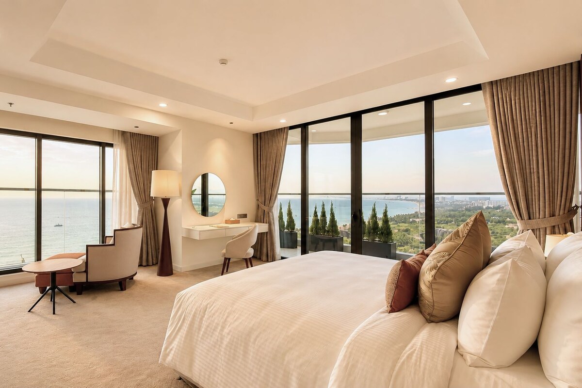 A hotel room with a large bed, a desk, a chair, and a view of the sea.