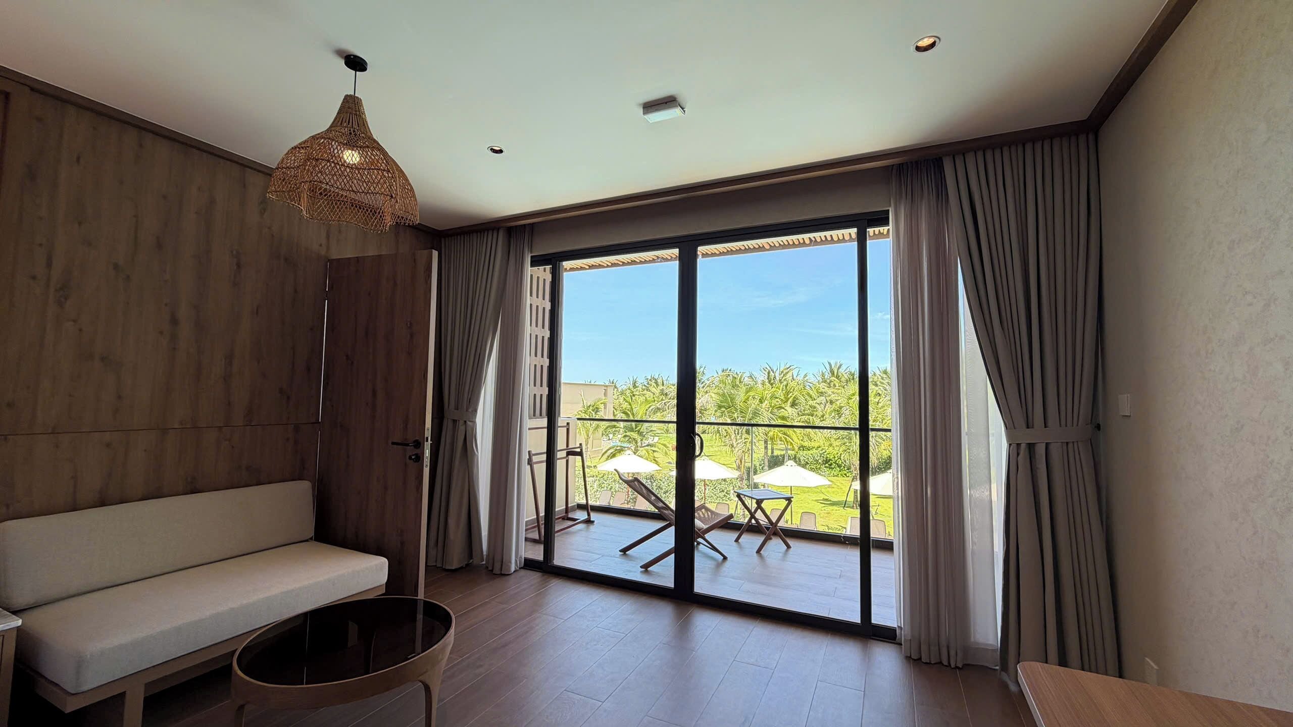 Une pièce moderne comprenant un canapé, une table ronde et une table à manger. Elle est dotée d’une grande porte-fenêtre coulissante qui donne sur un espace extérieur offrant une vue sur la verdure.