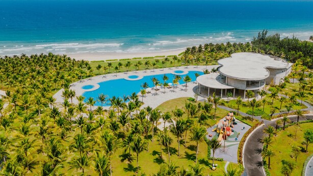 Vue aérienne d’un complexe hôtelier doté d’une grande piscine, de palmiers et d’une plage.