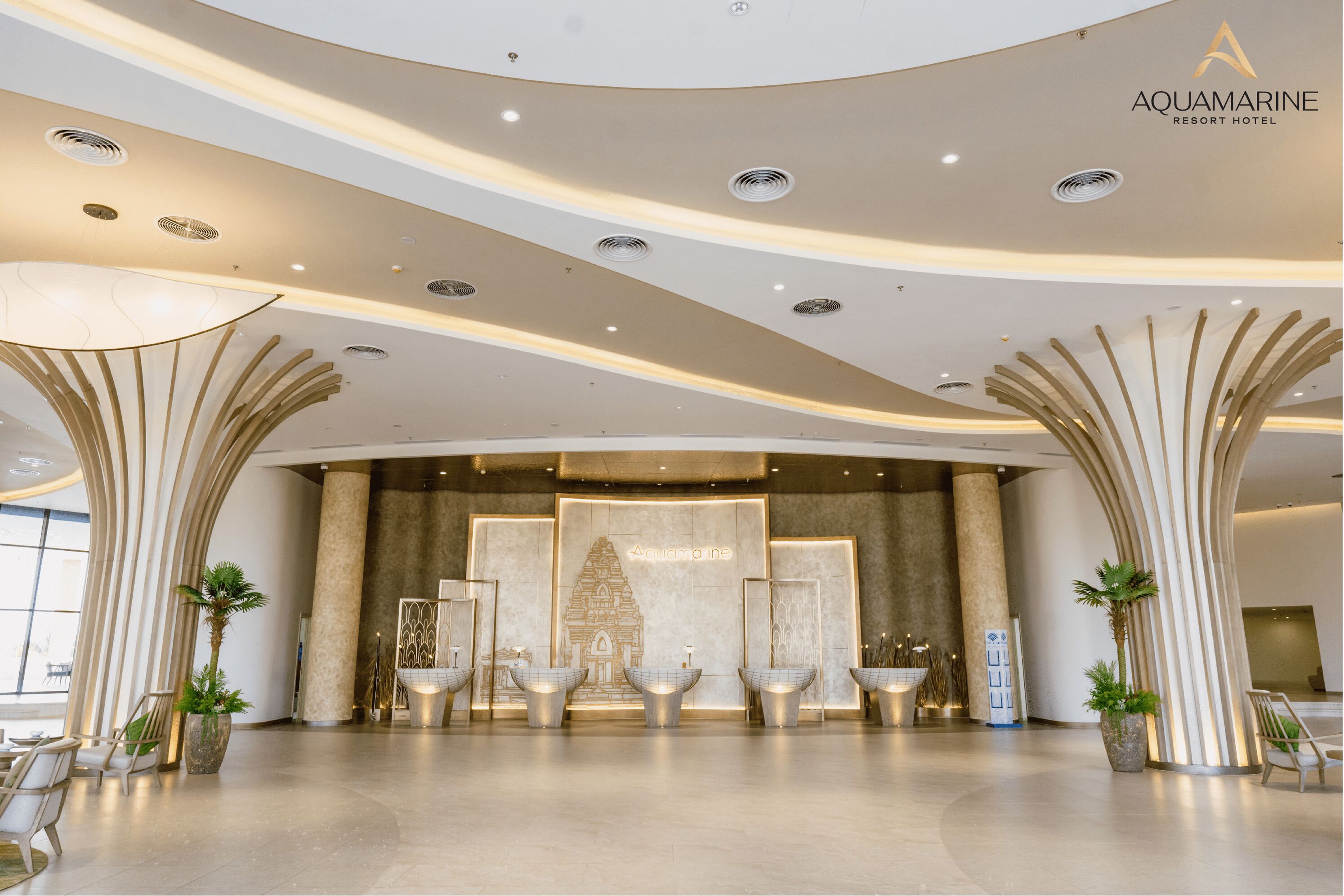 A modern hotel lobby with a central reception desk, decorative lighting, and a large mural.