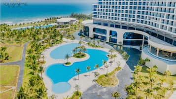 An aerial view of Aquamarine Resort Hotel with a large pool area, palm trees, and a view of the ocean.