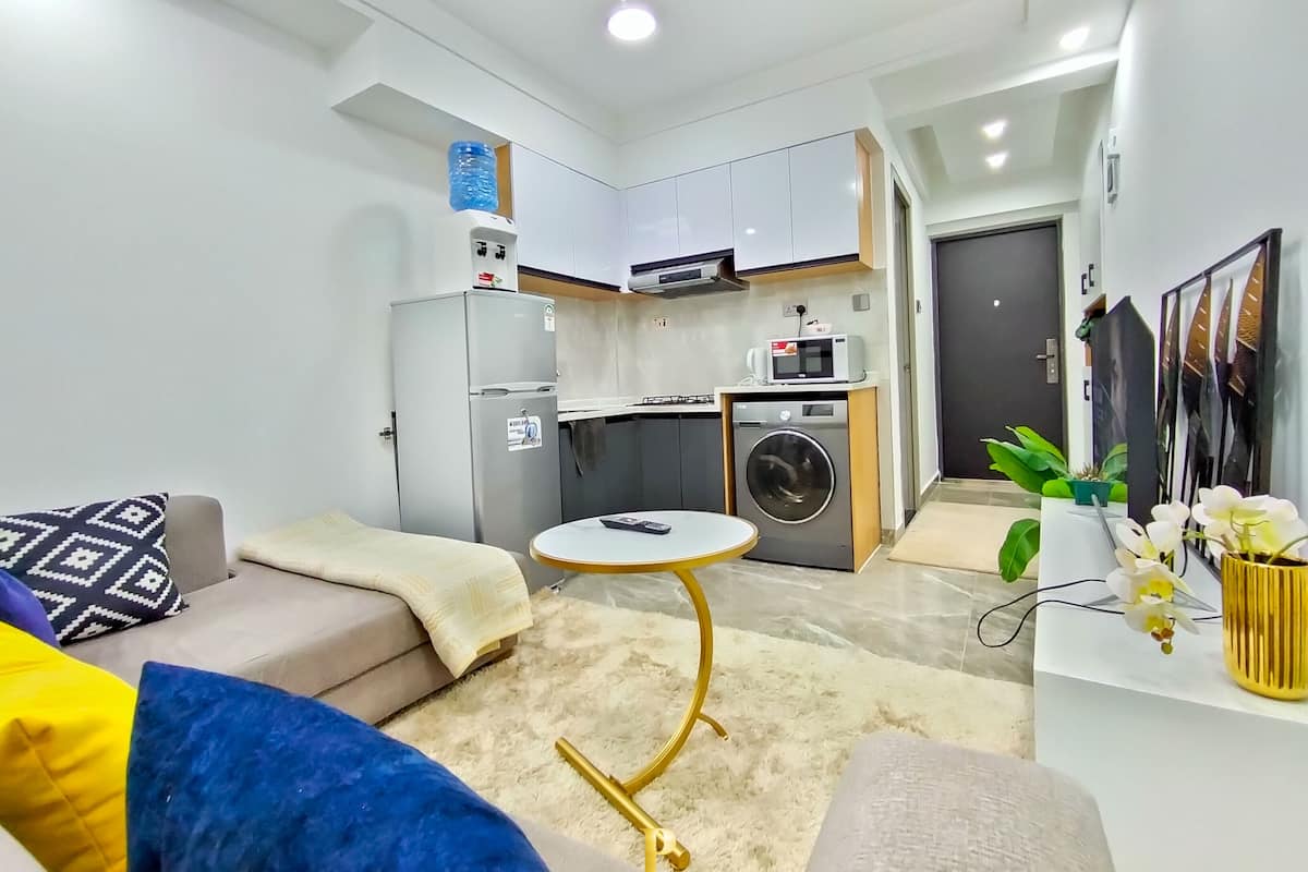 A compact living space with a kitchenette, a sofa, a small round table, and a washing machine.