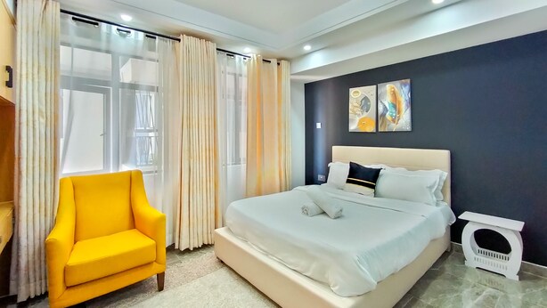 Un dormitorio moderno con una cama grande, un sillón amarillo y una mesita de noche pequeña.