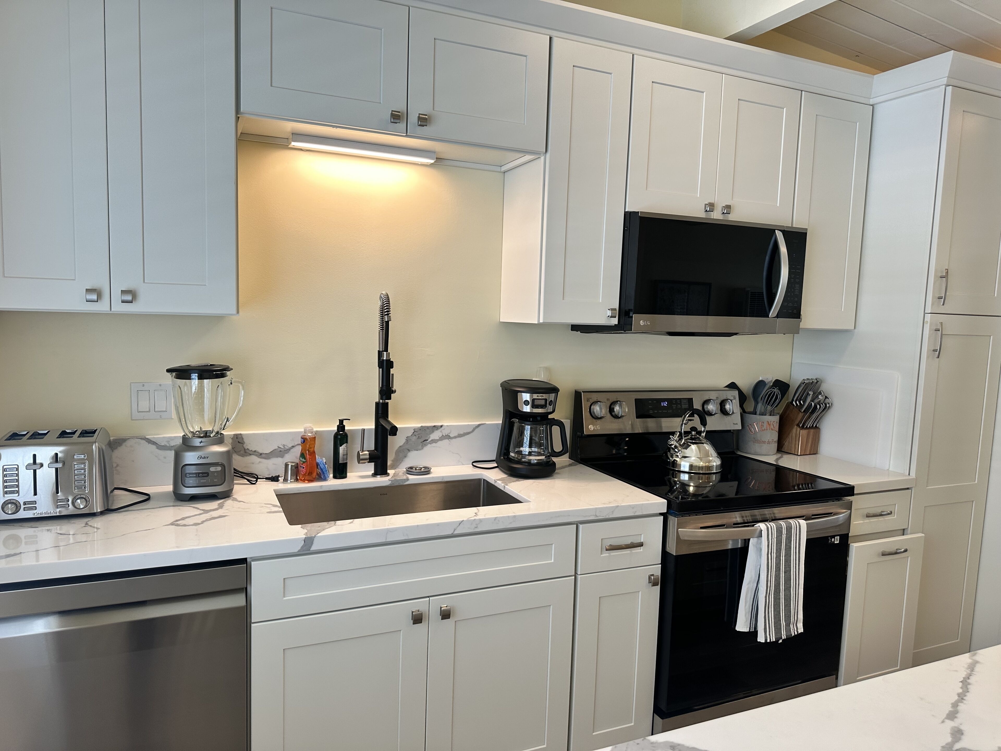 Una cocina moderna con armarios blancos, una estufa de acero inoxidable, un microondas, una cafetera y un tostador.