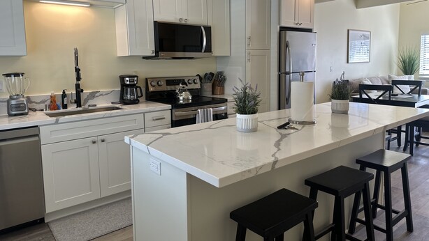 A modern kitchen with white cabinets, stainless steel appliances, and a marble countertop. - Coastal Haven Unbeatable Beach and Village Location  (Carlsbad)
