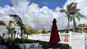 A patio area with outdoor furniture, a red umbrella, and a white fence. - Coastal Haven Unbeatable Beach and Village Location  (Carlsbad)