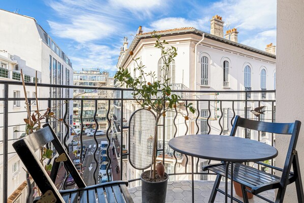 A balcony with a potted plant, a table, and two chairs.