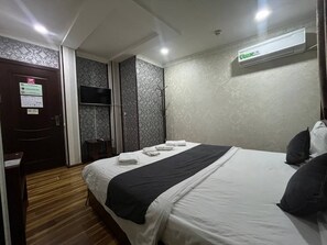 Quarto de hotel com cama, escrivaninha, guarda-roupa e ar condicionado.