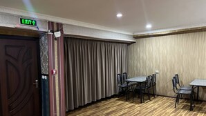 A conference room with a wooden floor, a table with chairs, a curtain, and an exit sign. - Sun Hotel Hostel (Tashkent)