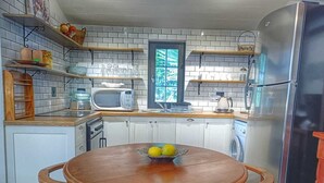 A kitchen with a round wooden table, a microwave, a refrigerator, and a window with a view. - Maison Dandelion (Franschhoek)