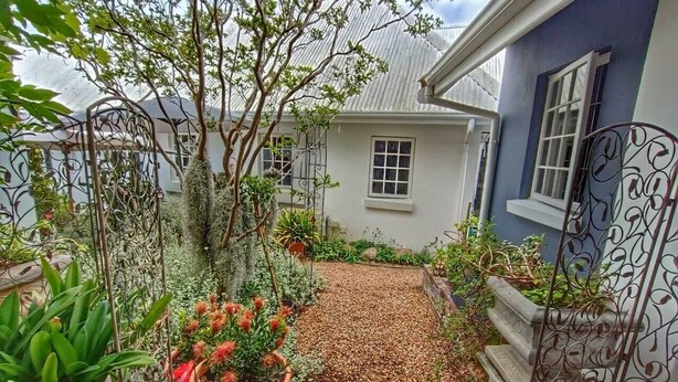 A garden with a brick pathway leading to a house with a blue exterior and white window frames. - Maison Dandelion (Franschhoek)