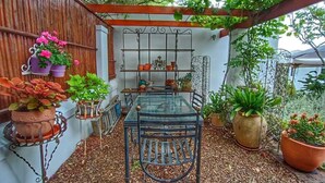 A covered patio with a glass table and metal chairs, surrounded by potted plants and a wooden fence. - Maison Dandelion (Franschhoek)