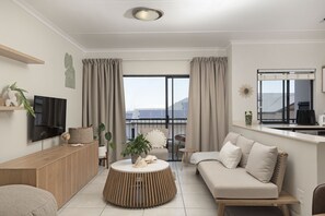 A modern living room with a sofa, a coffee table, a TV, and a balcony with curtains. - Ballito Hills Unit 79 (Ballito)