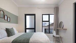 A bedroom with a large bed, a chair, a window, and a door leading to a balcony. - Ballito Hills Unit 79 (Ballito)