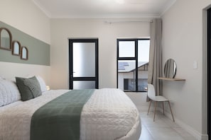 A bedroom with a large bed, a chair, a window, and a door leading to a balcony.