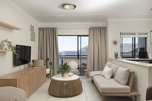 A modern living room with a sofa, a round wooden coffee table, a TV, and a balcony with curtains. - Ballito Hills Unit 79 (Ballito)