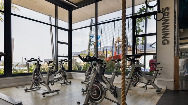 A gym with stationary bikes, large windows, and a view of a water park. - Ballito Hills Unit 79 (Ballito)