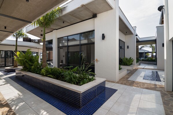 A modern building with a covered outdoor area featuring tiled flooring, planters with greenery, and a clear view of the sky.