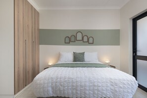 A bedroom with a large bed, wooden wardrobe, and a wall-mounted light fixture.