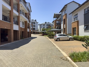 A residential street with modern apartment buildings, a paved road, and a parked car.