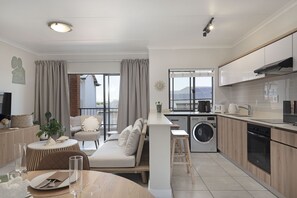 A modern apartment with a kitchenette, a dining area, a living room with a sofa, and a balcony with curtains. - Ballito Hills Unit 79 (Ballito)
