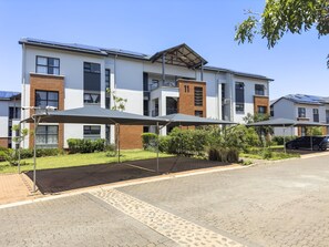 A modern residential building with multiple balconies, solar panels, and covered outdoor seating areas.