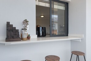 A balcony with a white shelf holding decorative items, a potted plant, and a coffee maker.