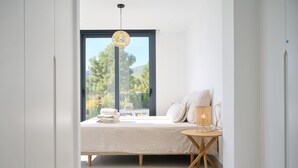 A modern bedroom with a large window, a bed with a white duvet, a bedside table with a lamp, and a view of greenery outside. - Casa Palmera - Polop, Costa Blanca (Polop)