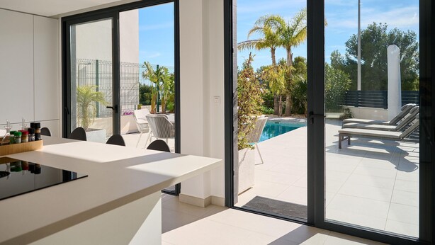 A modern kitchen with a large island, sliding glass doors leading to a pool area with lounge chairs. - Casa Palmera - Polop, Costa Blanca (Polop)