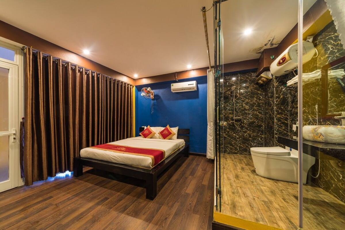 A hotel room with a bed, a shower area, and an air conditioning unit.