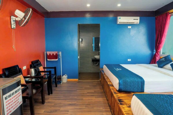 Habitación de hotel con cama, escritorio con silla, una mesita, microondas y equipo de aire acondicionado.