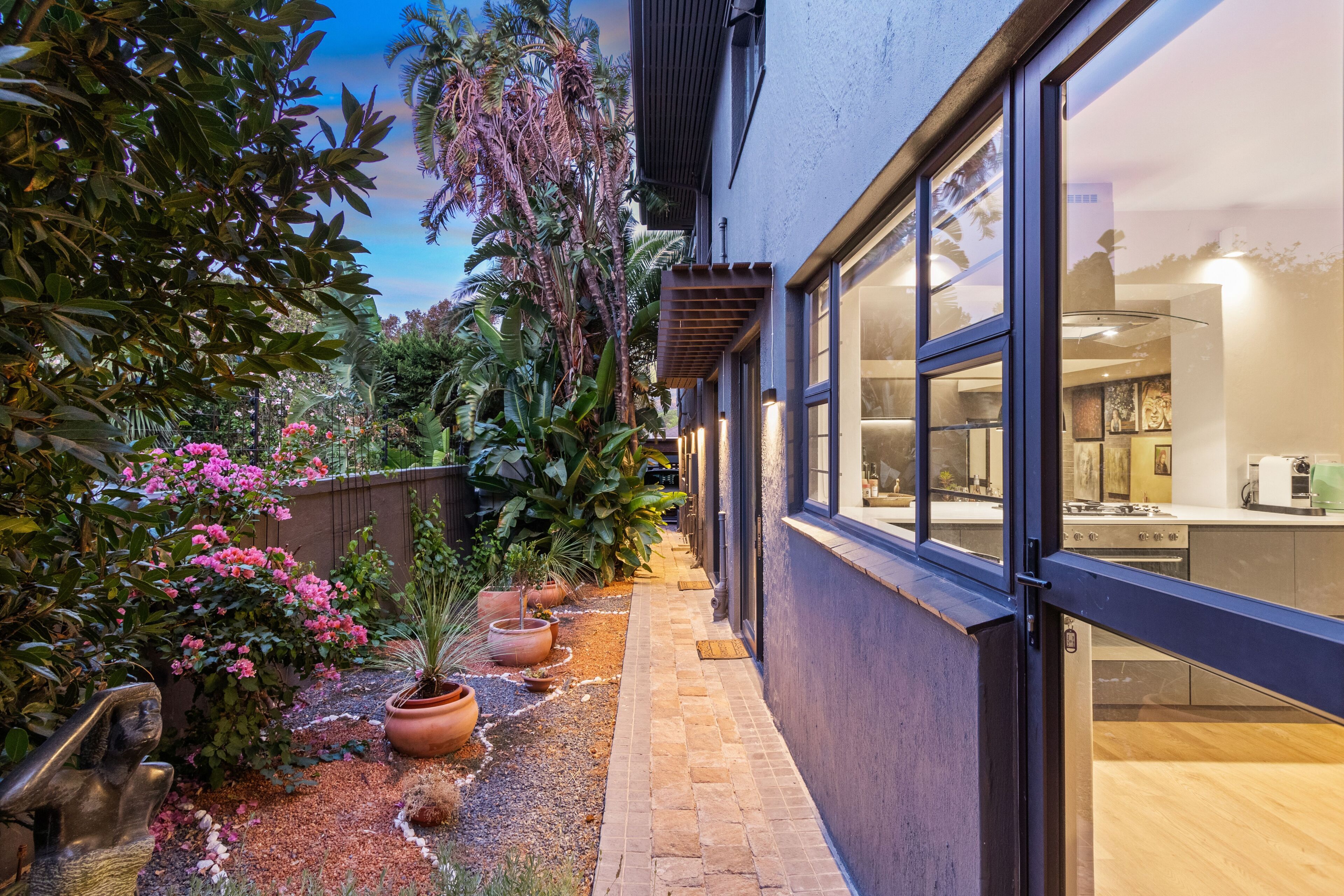 A modern kitchen with large windows, a stone pathway, and lush greenery.