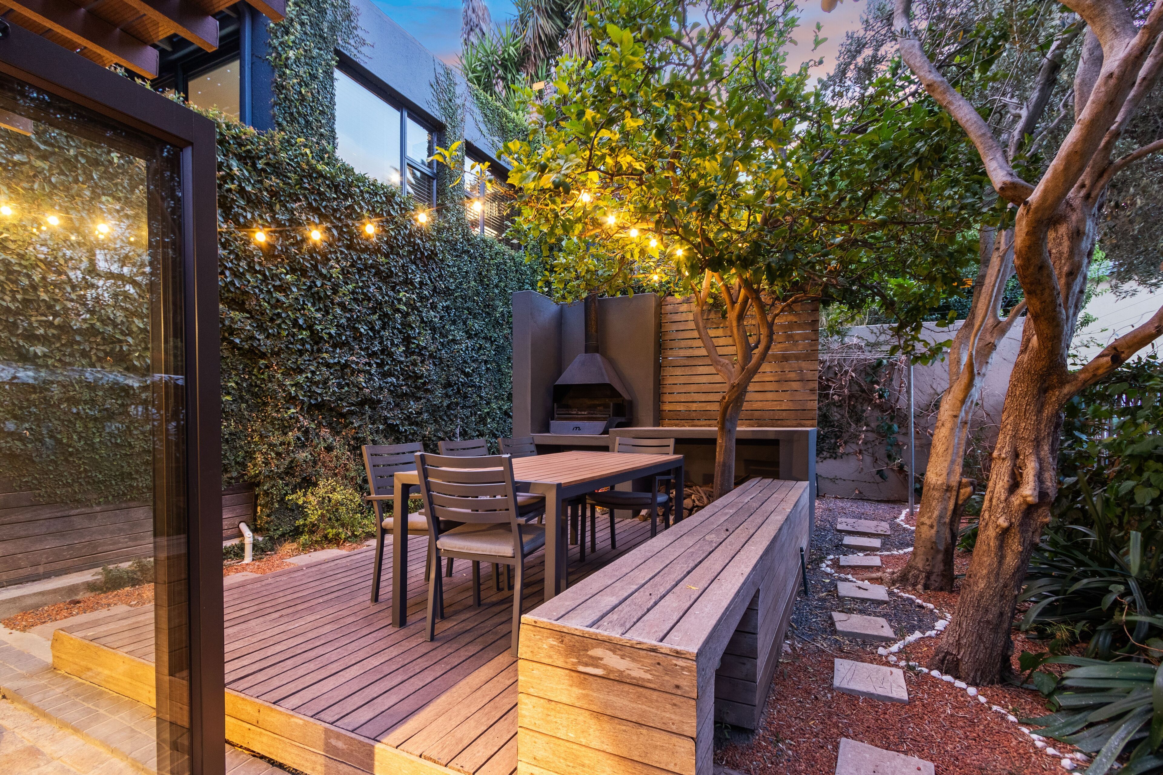An outdoor patio with a wooden deck, a built-in bench, and a table with chairs.