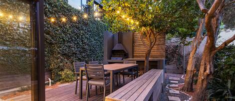 An outdoor patio with a wooden deck, a built-in bench, and a table with chairs.