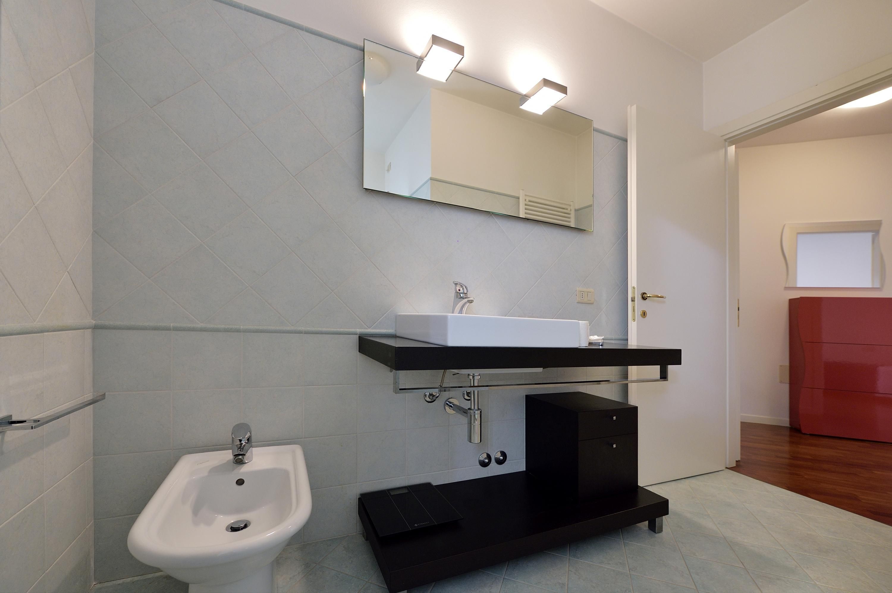 A modern bathroom with a white sink, bidet, and a large mirror with integrated lighting.