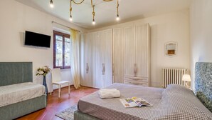 A bedroom with a bed, a sofa, a TV, a wardrobe, and a window. - Quercia 1 - Relax in Tuscany (Montaione)