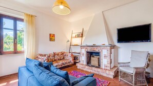 A living room with a sofa, a chair, a fireplace, a television, and a bookshelf. - Quercia 1 - Relax in Tuscany (Montaione)