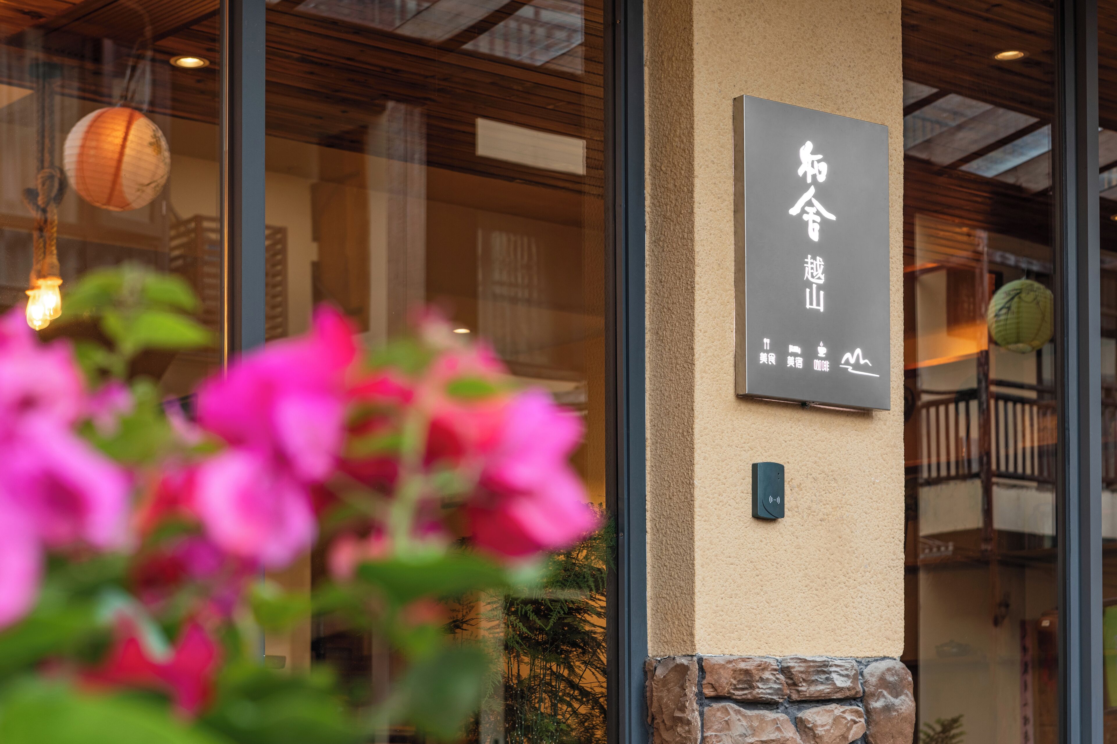 A building entrance with a sign in a foreign language, a stone wall, and a hanging light fixture.