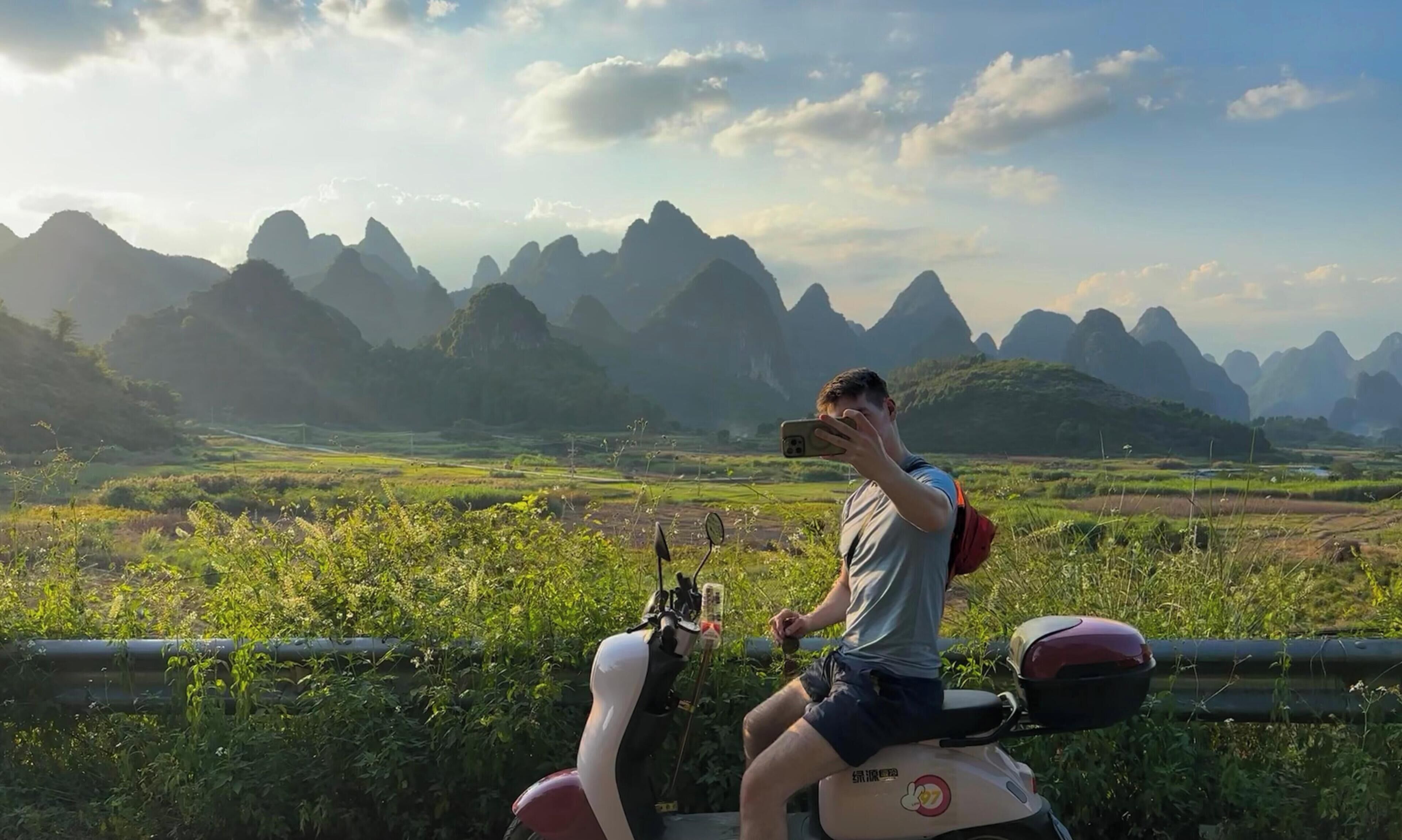 Une personne sur un scooter, avec un paysage montagneux pittoresque en arrière-plan.