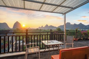 Un balcón con mesa y sillas, con vistas a un paisaje montañoso durante el atardecer.