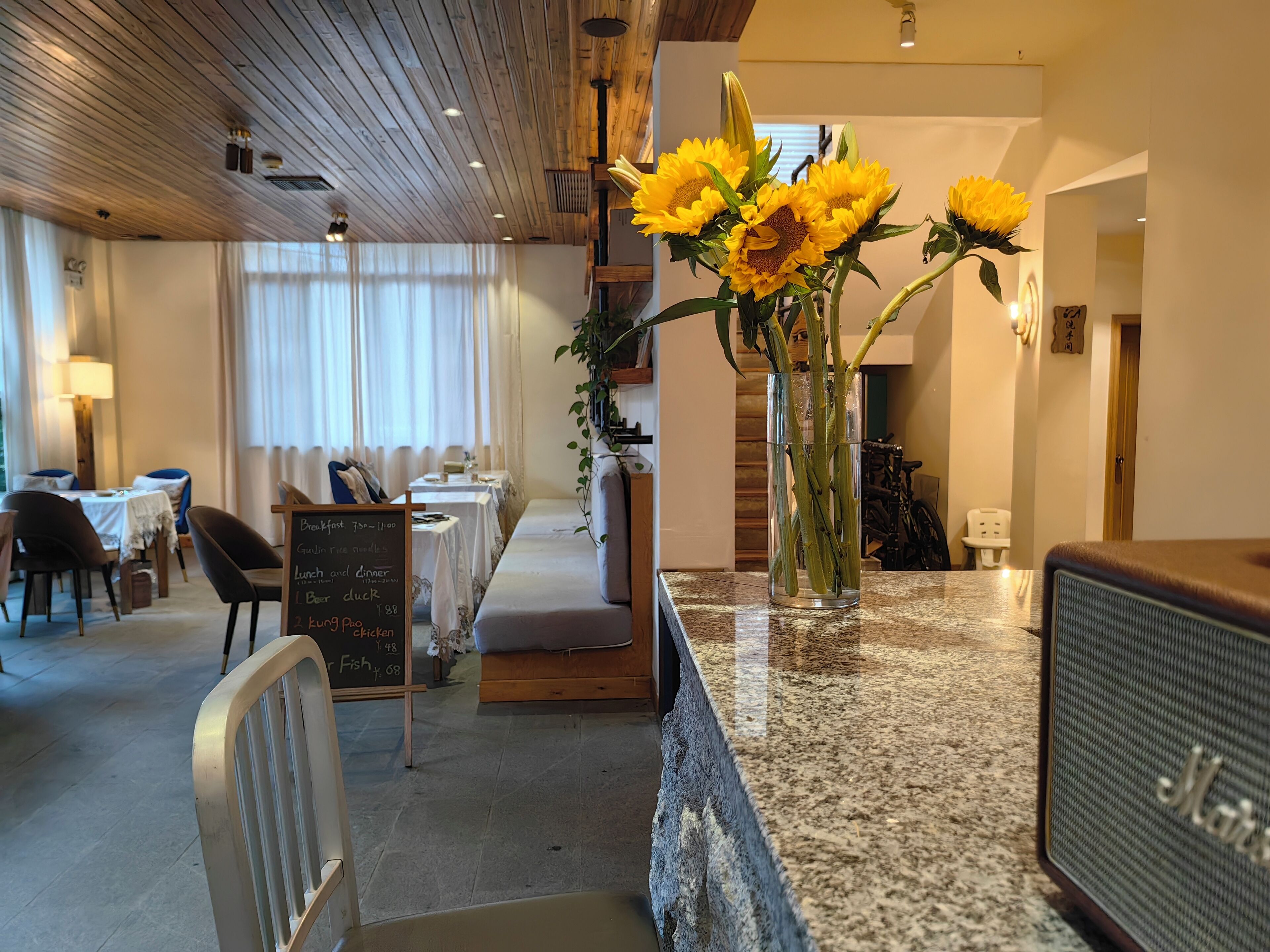 En restaurant med træloft, tavlemenu og en vase med solsikker på disken.