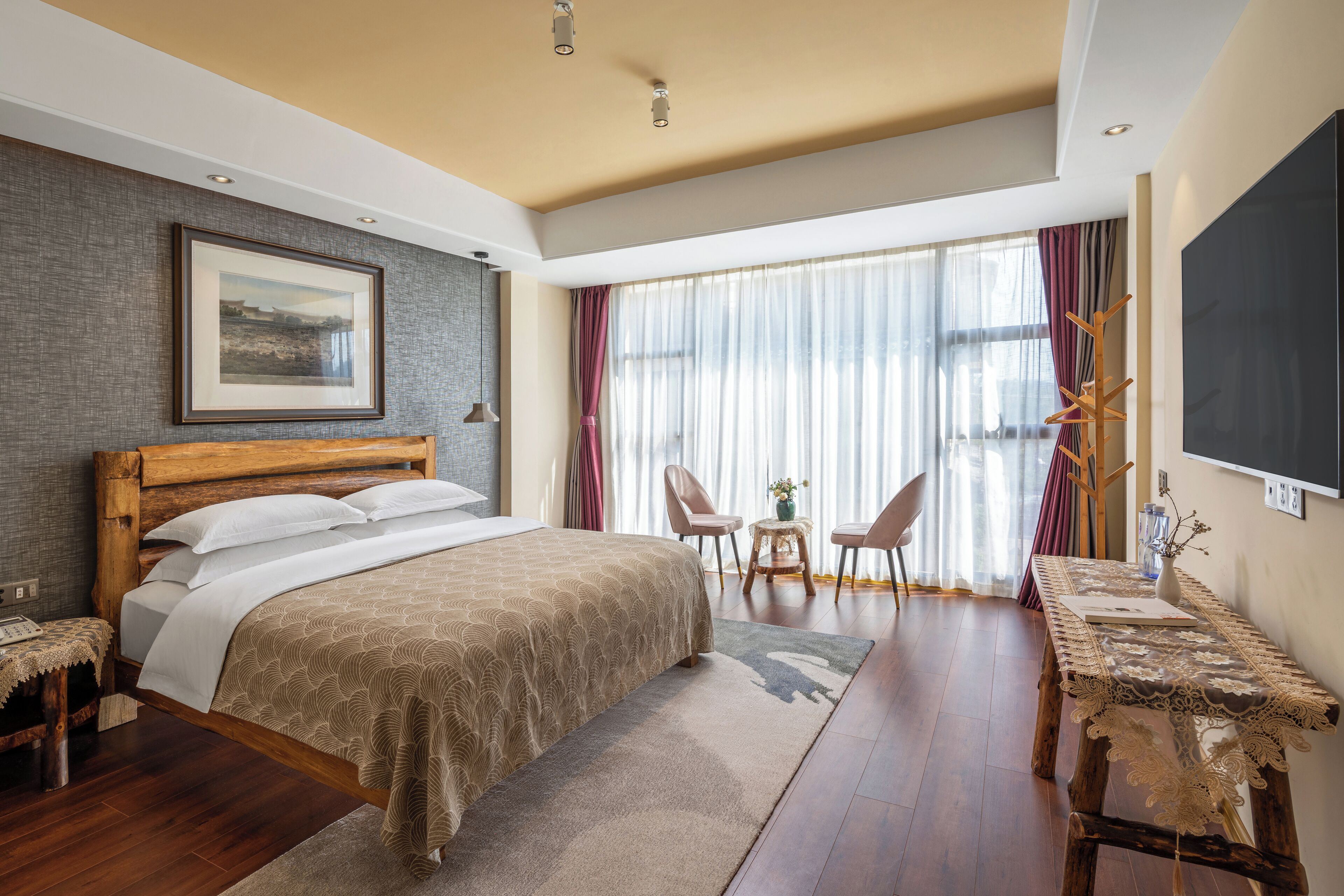 A bedroom with a bed, bedside table, chairs, a table, a TV, and a window with curtains.