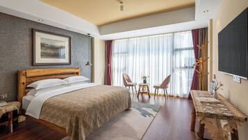 A bedroom with a bed, bedside table, chairs, a table, a TV, and a window with curtains.