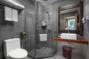 Un baño moderno con cabina de ducha de vidrio, un inodoro blanco, un tocador de madera con lavabo y un espejo con marco de madera.