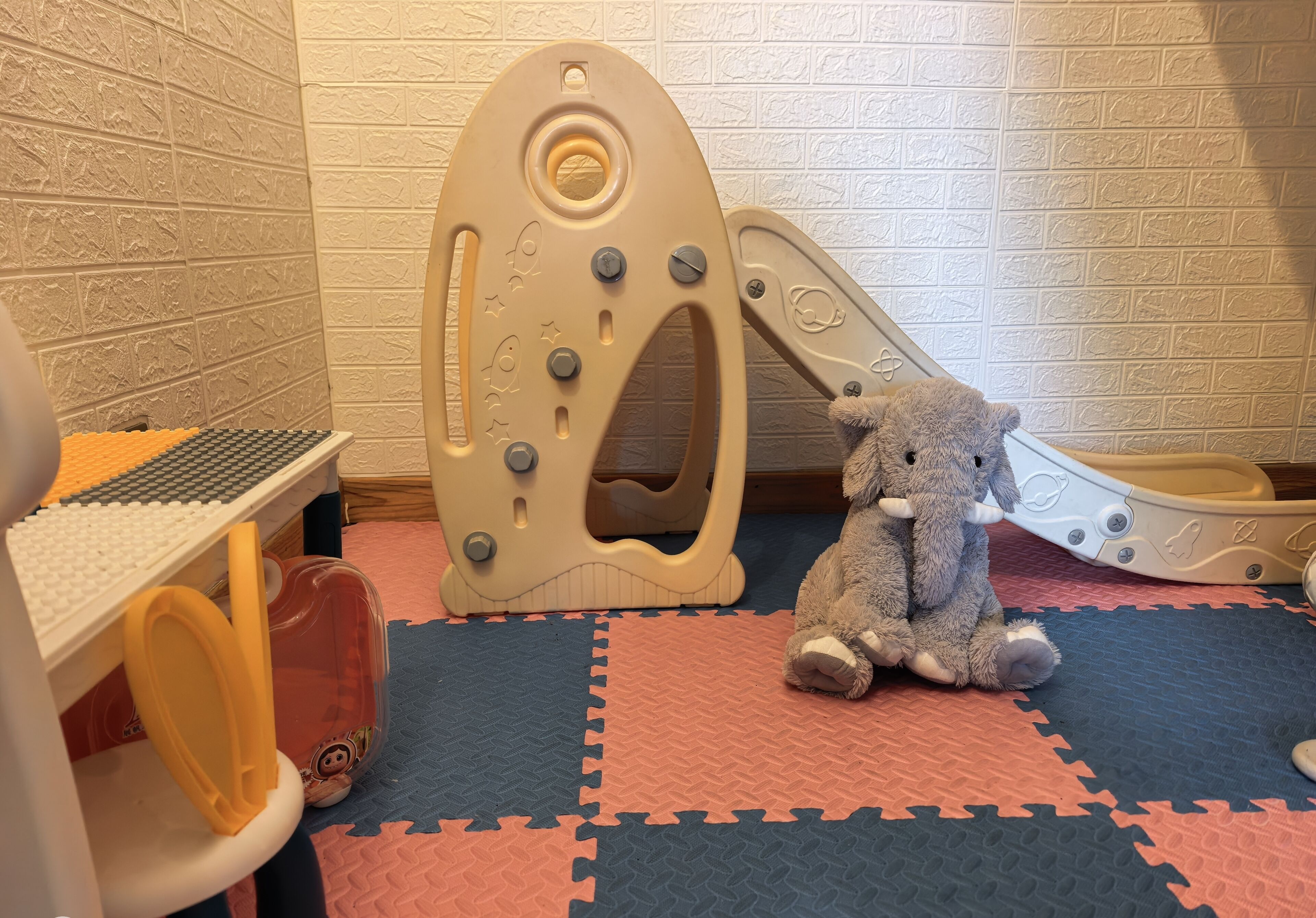 Un espace de jeux avec un toboggan, une voiture jouet et un tapis de jeu souple.