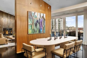 A modern living room with a large abstract painting, a fireplace, and a dining area with a round table and chairs. - Luxury Penthouse Living, Breathtaking Views, Huge Wraparound Deck, All New Decor, Two Parking Spots (Portland)