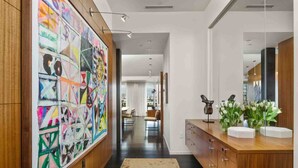 A modern bathroom with a wooden vanity, a large mirror, and a colorful abstract painting on the wall. - Luxury Penthouse Living, Breathtaking Views, Huge Wraparound Deck, All New Decor, Two Parking Spots (Portland)