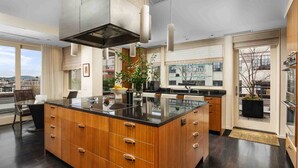 A modern kitchen with a central island, wooden cabinets, and a large window offering a city view. - Luxury Penthouse Living, Breathtaking Views, Huge Wraparound Deck, All New Decor, Two Parking Spots (Portland)