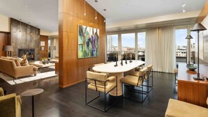 A modern living room with a fireplace, a large abstract painting, and a dining area with a round table and chairs. - Luxury Penthouse Living, Breathtaking Views, Huge Wraparound Deck, All New Decor, Two Parking Spots (Portland)
