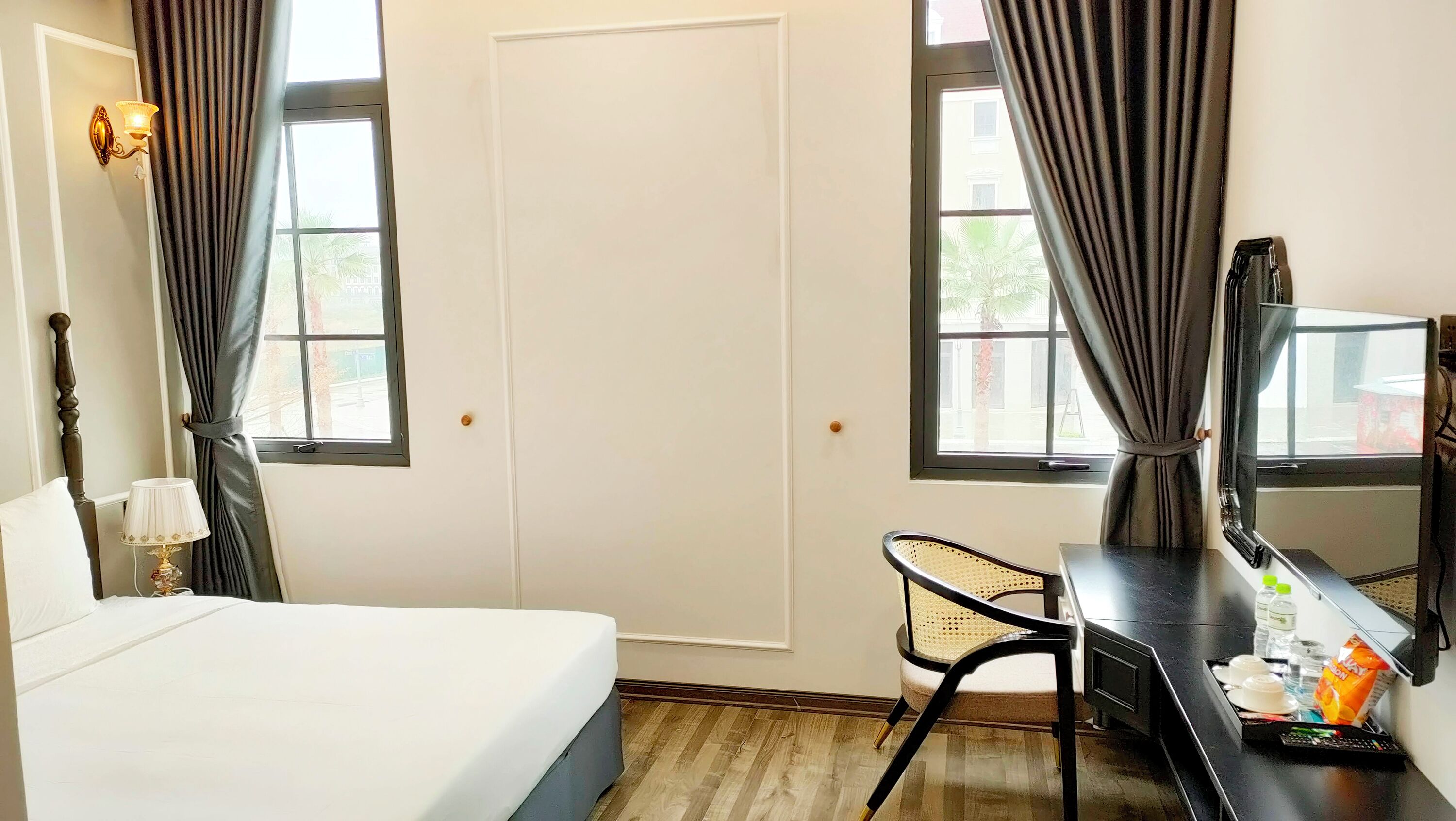 A hotel room with a bed, a desk with a chair, a television, and a window with curtains.